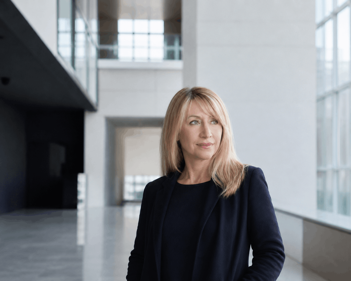 An advisor standing in a daylit concrete and glass building, looking thoughtfully into the distance