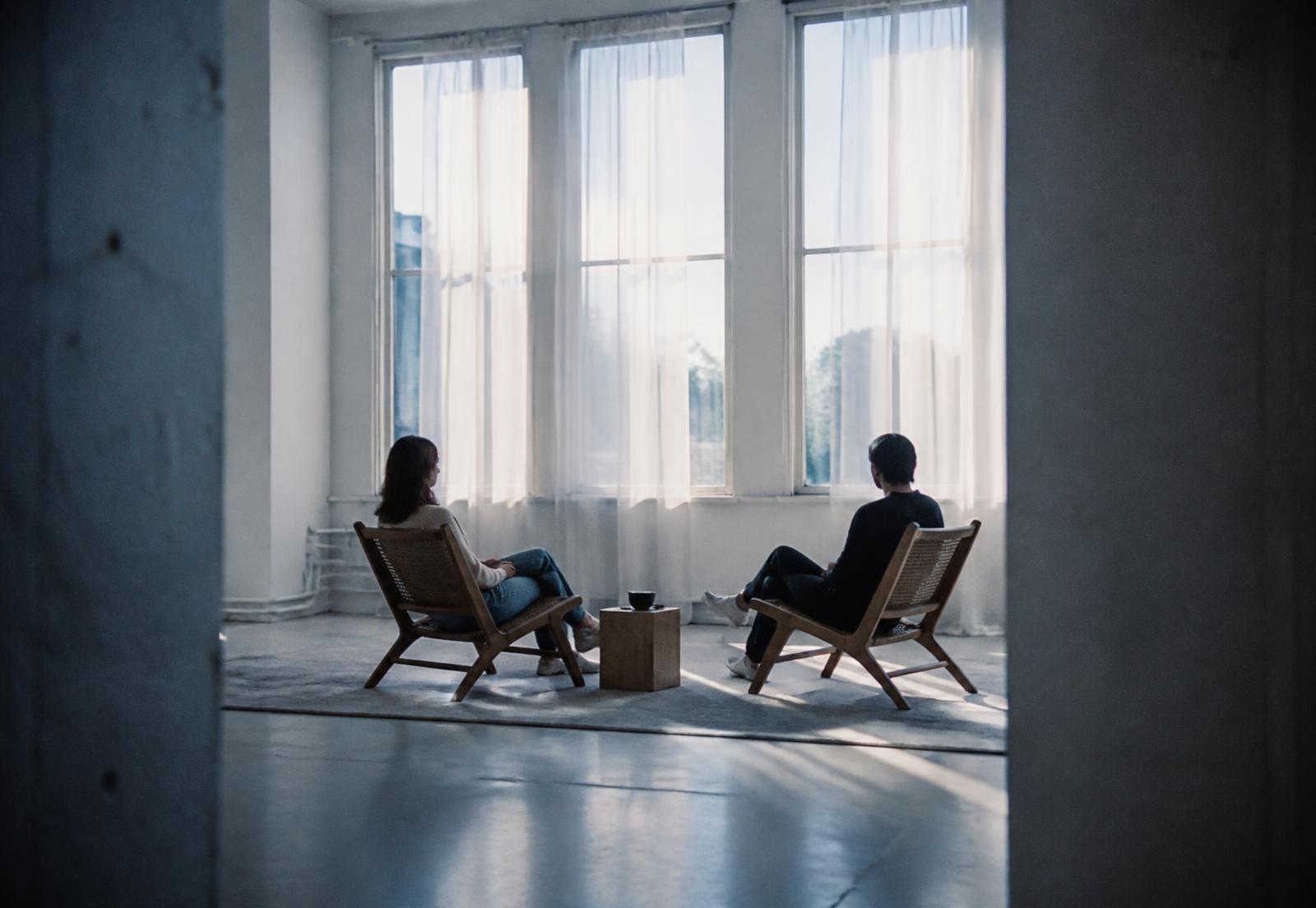 Two people seated in conversation across a bright room filled with daylight